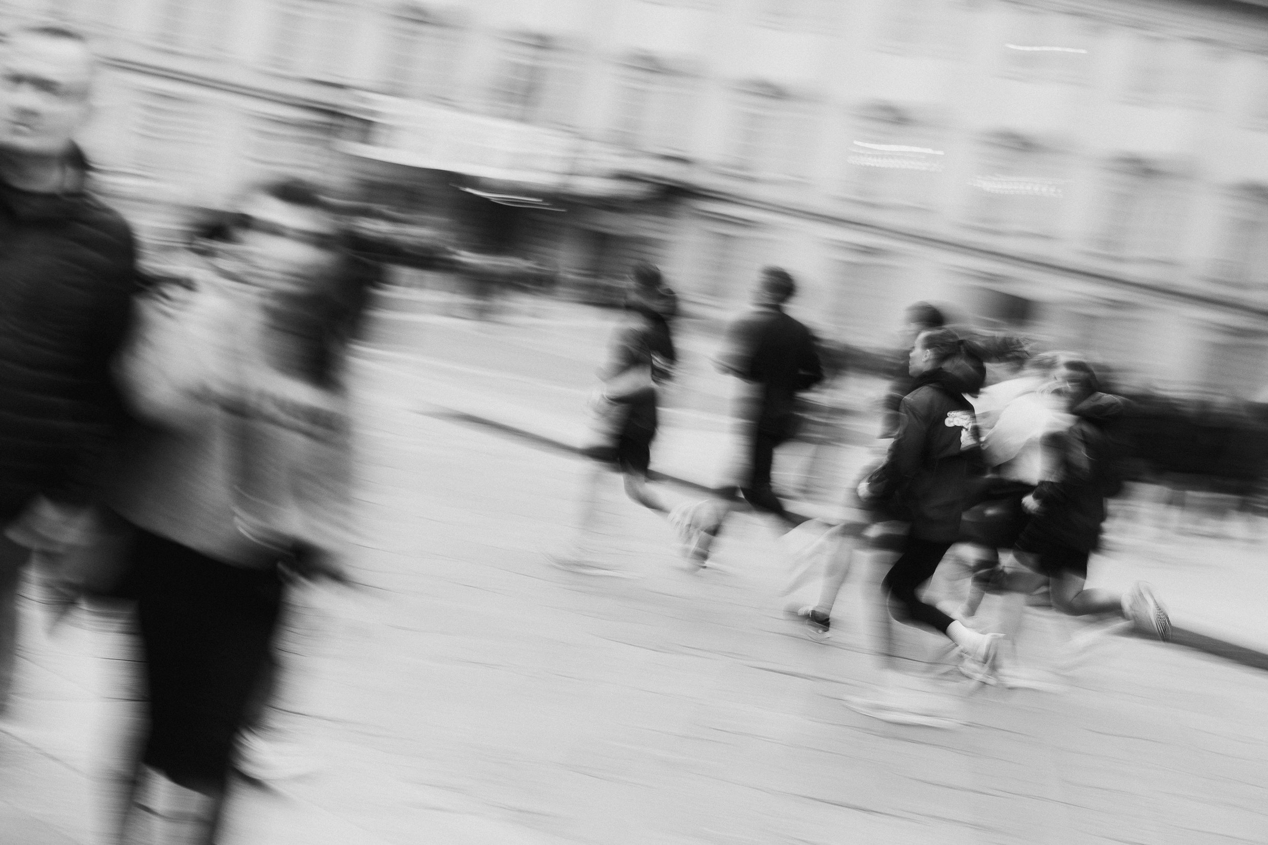 Blurred black and white photo of people running on a city street.