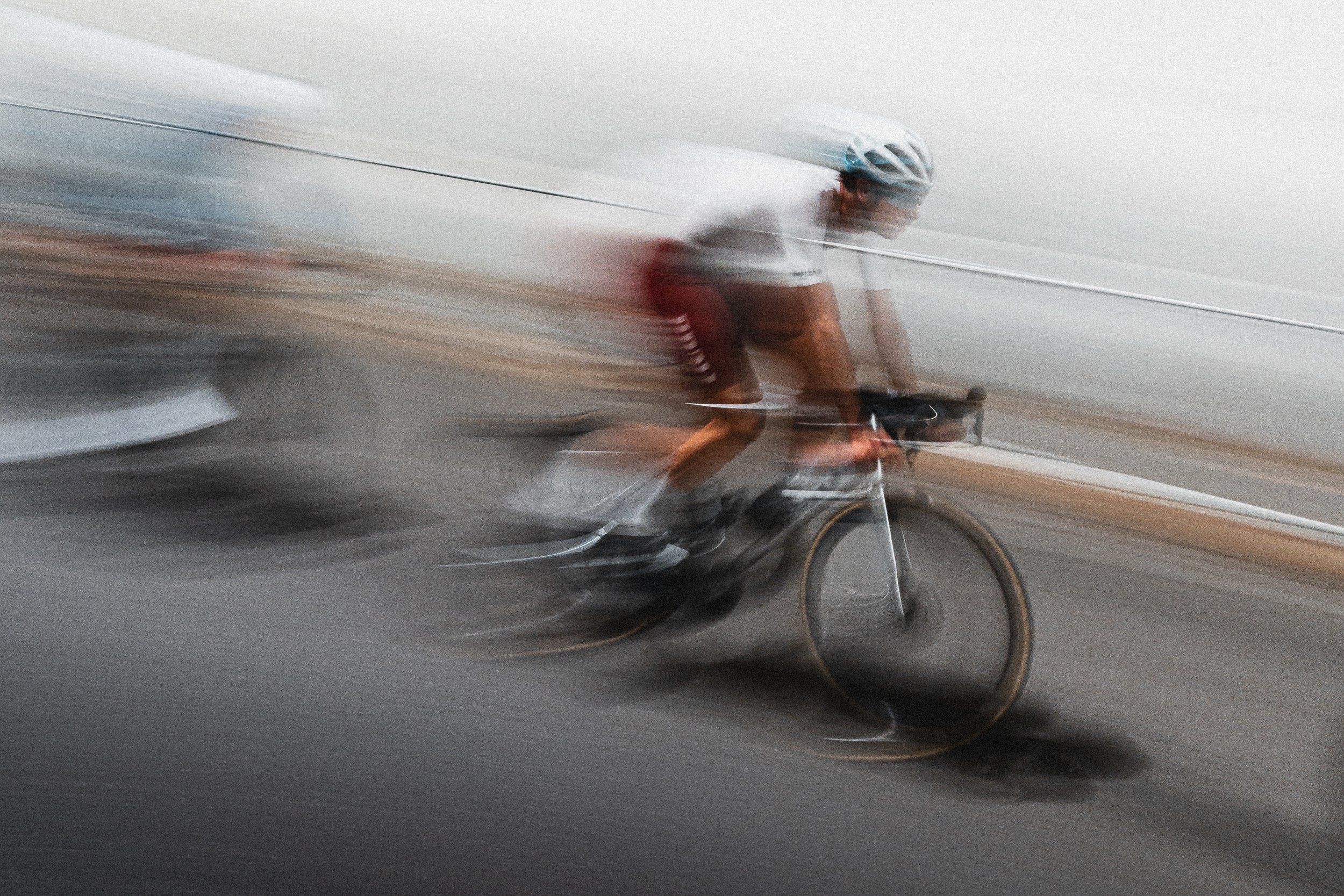 A cyclist wearing a helmet riding a bicycle on a road, captured with motion blur.